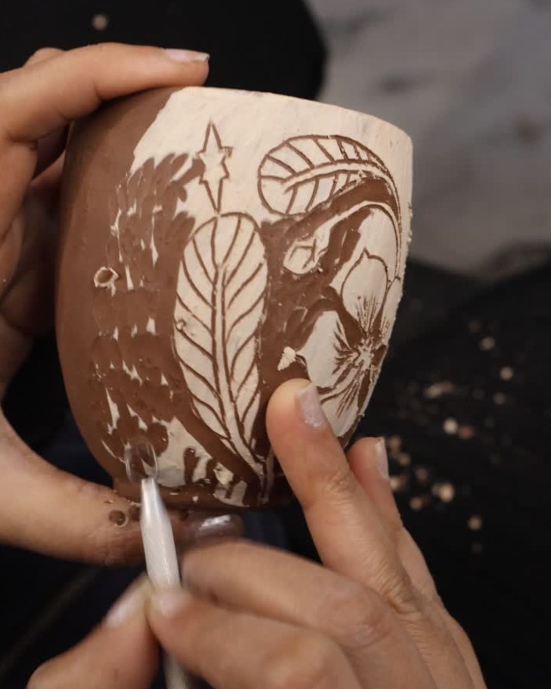 Hands carving a flower and leaf design into a terracotta kulhad